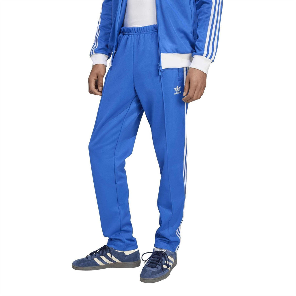 Blue adidas track pants with white side stripes and zip pocket detail