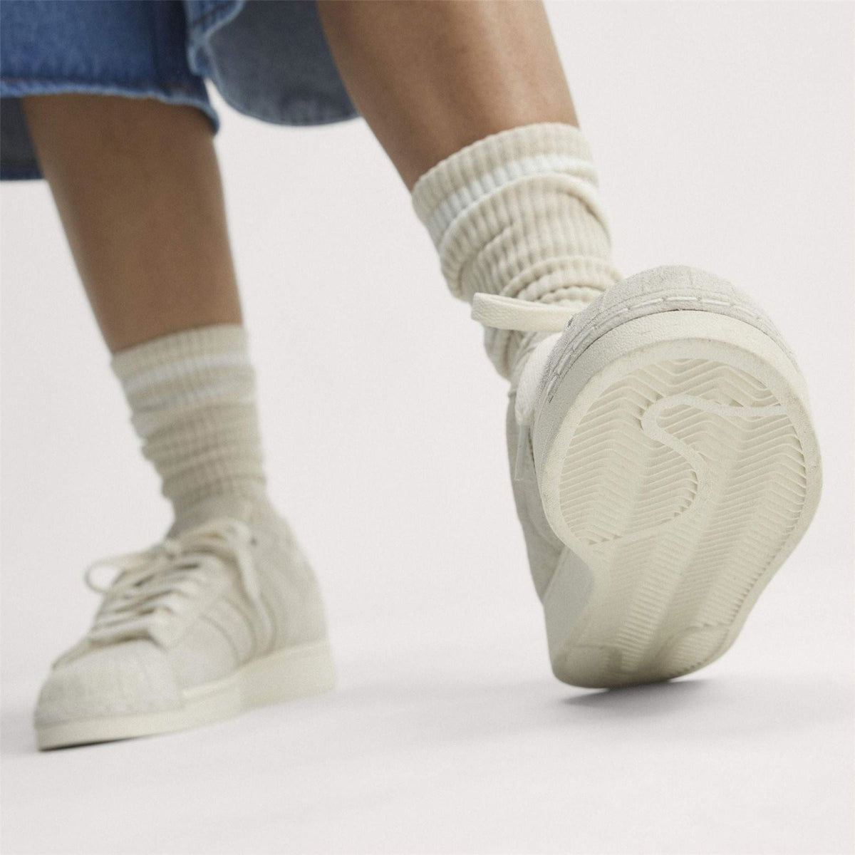 Light cream sneakers on model feet with ribbed crew socks and lace-up front