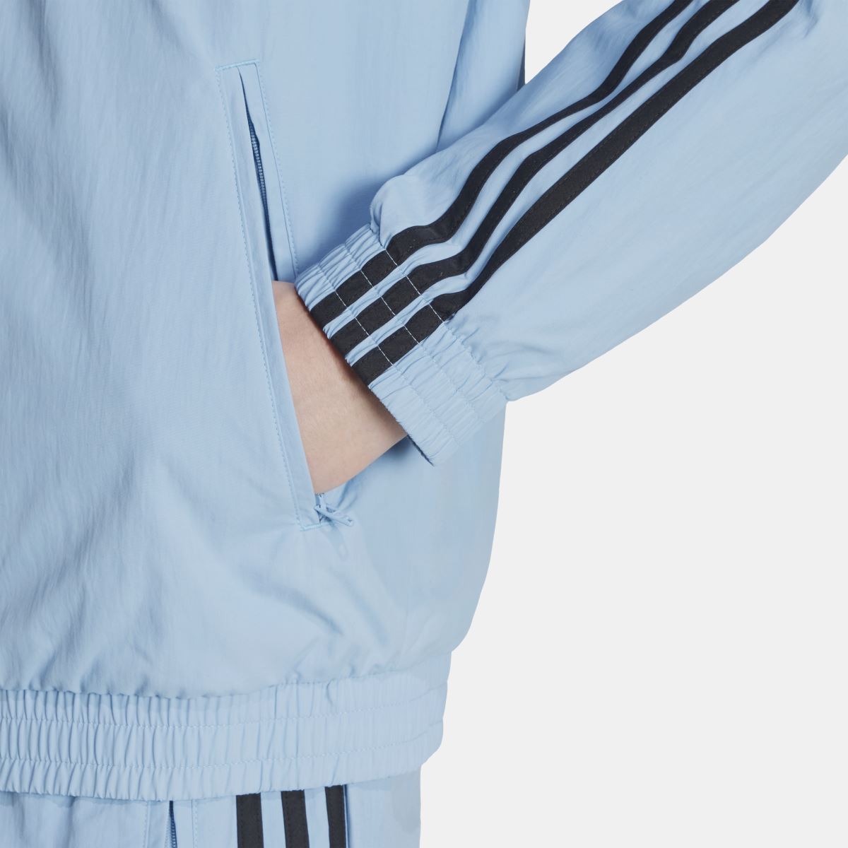 Light blue track top cuff detail with black triple stripe sleeve accents and zip front