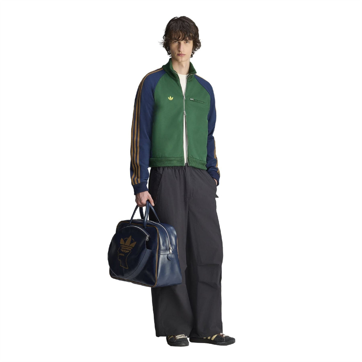 Green track jacket with gold stripe sleeves, full zipper, worn with a navy duffel bag