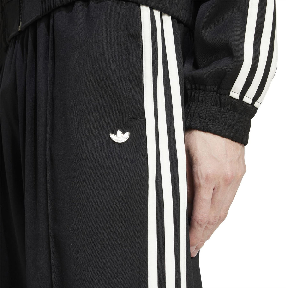 Black track pants detail with small adidas trefoil logo and side white stripe panel