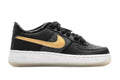 Kids low-top sneakers in black with gold swoosh, white sole, and black laces